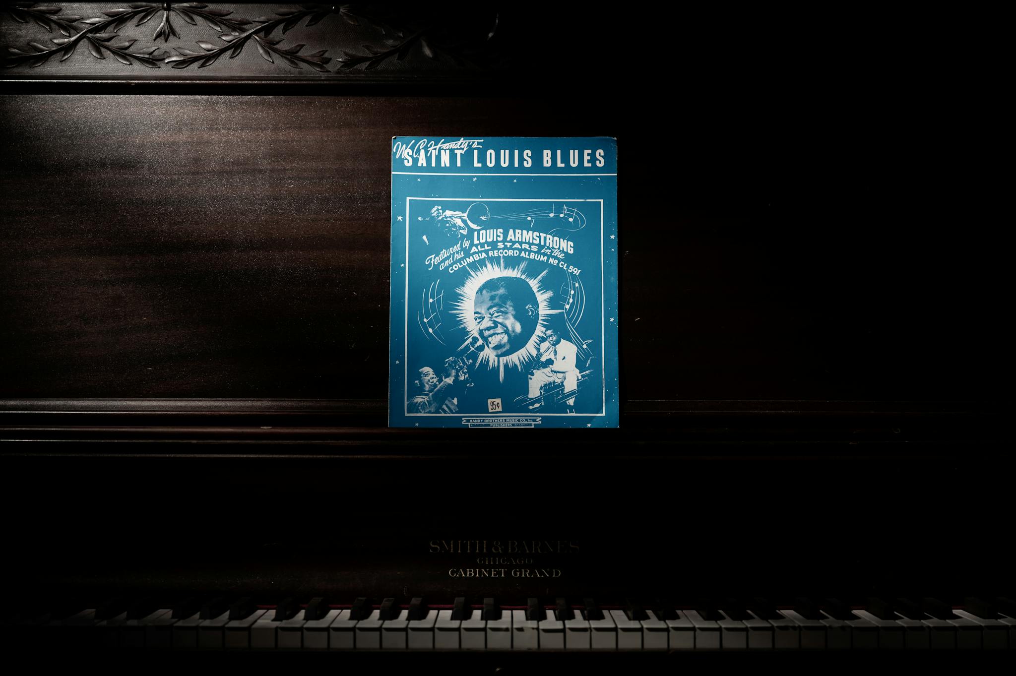 A vintage 'Saint Louis Blues' sheet music by Louis Armstrong displayed on a classic piano.