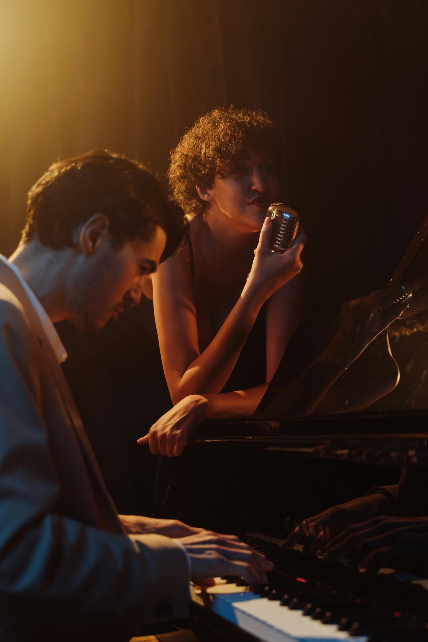 Emotive jazz duo performing with piano and vintage microphone under warm stage lighting.